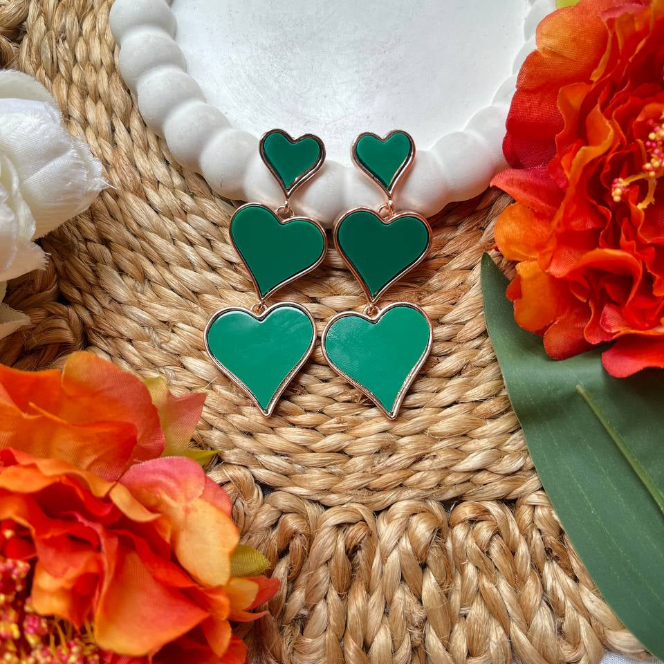 Green heart-shaped earrings on a woven mat with orange flowers
