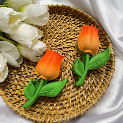 Two orange tulip-shaped cookies on a woven mat with white tulips.